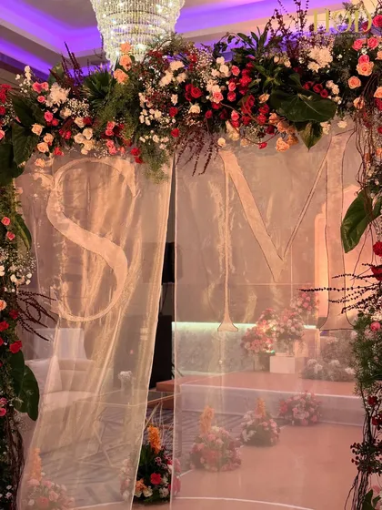 A close-up of the couple's initials 'S' and 'M' on the sheer curtain under the floral arch, a beautiful example of personalized wedding decor.