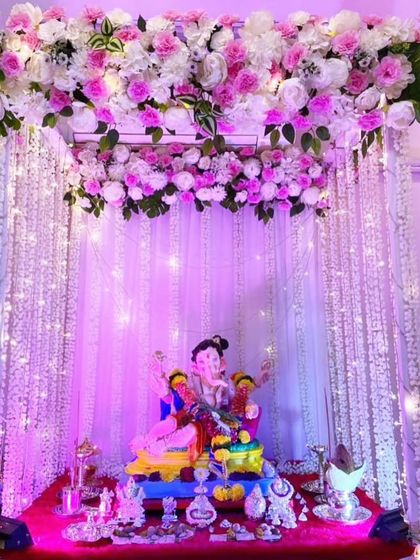 A stunning mandap with a ceiling of pink and white flowers and curtains of hanging white flower strings. The purple lighting gives it a magical, ethereal glow.