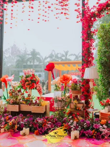 A panorama of a whimsical Mehendi setup, filled with oversized paper flowers, a ceiling of hanging petals, and countless floral arrangements. It's a true floral wonderland.