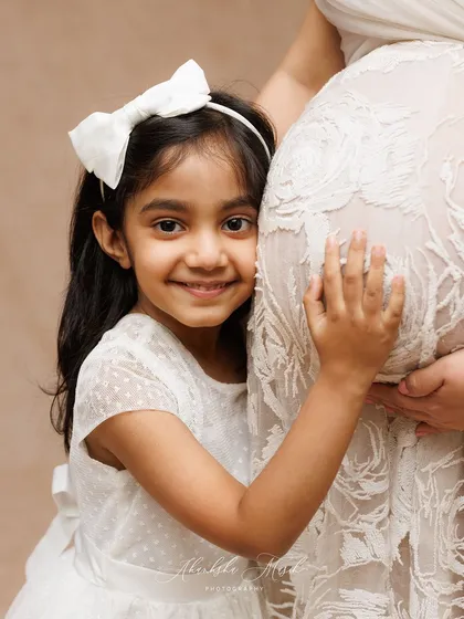 A daughter's sweet embrace for her mother's growing belly. Including older siblings in maternity photos is a wonderful way to capture the family's shared excitement.