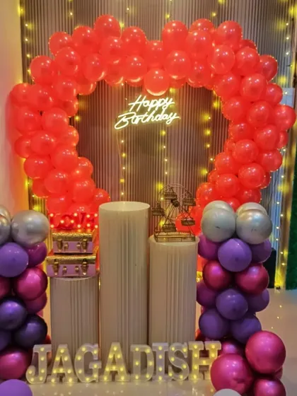 A heart-shaped balloon arch made entirely of red balloons for a bold birthday statement. The name "JAGADISH" is spelled out in light-up letters at the base.