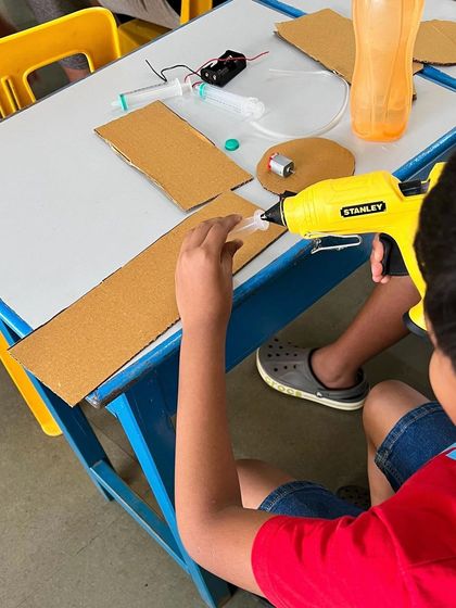A child carefully applies hot glue to their cardboard construction. The glue gun is one of the most versatile tools in our Tinker Den.