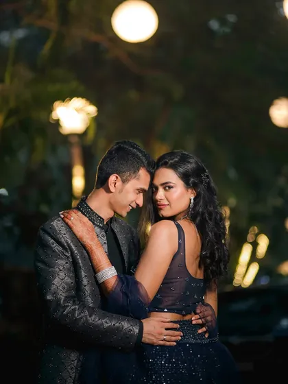 A captivating portrait where the bride looks directly at the camera while embraced by her groom. The soft bokeh of the background lights adds a dreamy quality to this intimate and confident night shot.