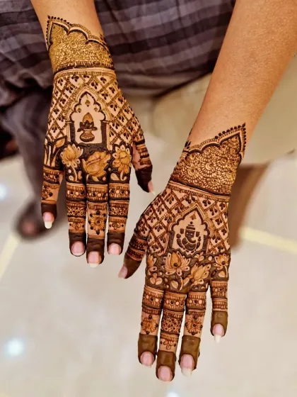 A festive fusion design incorporating Lord Ganesha and a kalash (holy pot) into the palms. The hands are filled with lotus motifs and geometric grids.