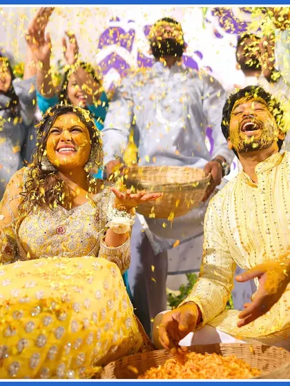 The couple laughing as they are completely covered in flower petals. A perfect candid shot from their Haldi.