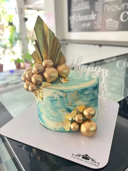 A marbled blue and white cake with gold leaf and a cascade of gold spheres.