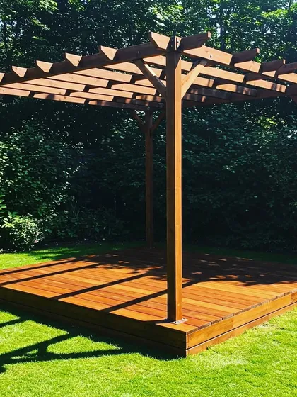 A freestanding wooden pergola with a matching raised deck, set in a sunny corner of a lawn. This simple, elegant structure is ready to be furnished as a yoga platform, lounge, or dining spot.