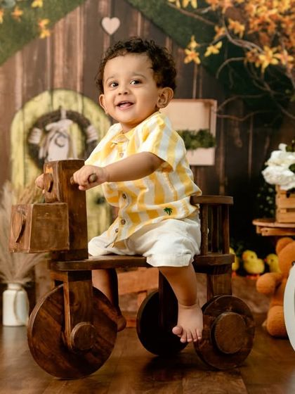 A cheerful farm-themed first birthday shoot, with a happy toddler on a wooden tractor.