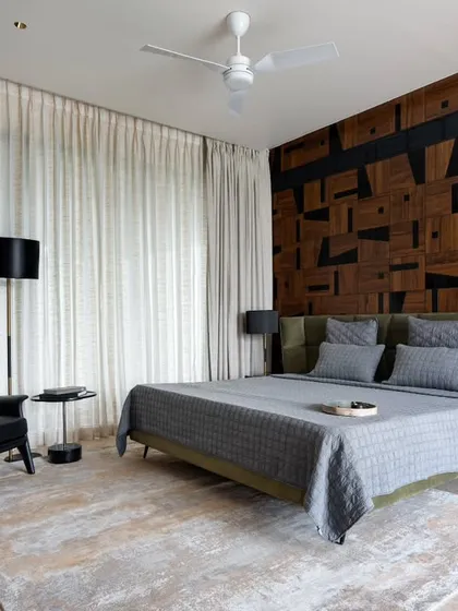 This bedroom in the Celadon residence features a unique accent wall made of reclaimed wood in a geometric pattern. We paired this rustic element with a modern olive green headboard, a classic black leather armchair, and soft, neutral textiles to create a balanced and tranquil space.