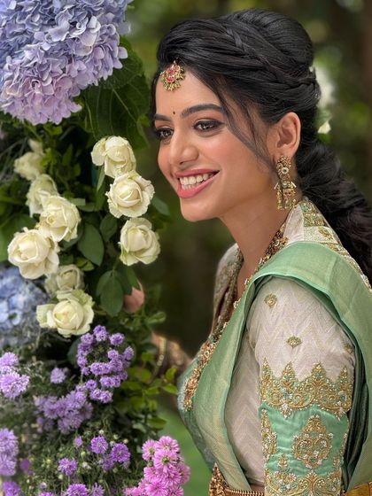 A happy bride surrounded by flowers. Her makeup is fresh and glowing, with a beautiful smile that lights up the photo.