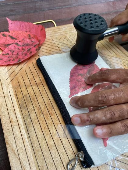 Here you can see the process of pounding a bright red leaf onto a cotton canvas pouch. This technique, called Tataki Zome, creates a beautiful and permanent botanical print.