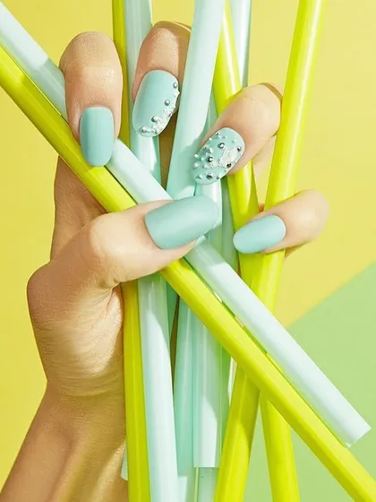 A close-up of a hand with a fresh, mint-green manicure holding matching straws. The bright, color-coordinated styling creates a fun, summery, and visually pleasing image.