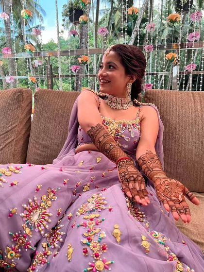 A beautiful bride in a purple lehenga, proudly displaying her full-arm mehandi.