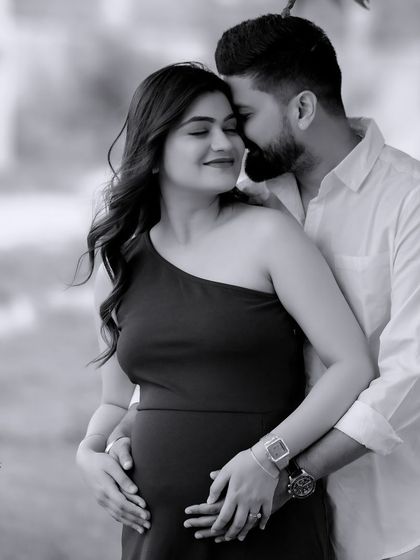 A timeless black and white photo of an expecting couple sharing a quiet moment outdoors.