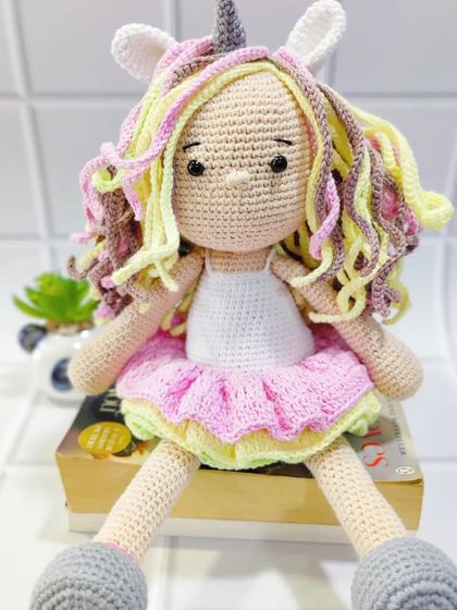 My unicorn doll sitting on a book, ready for story time. It shows her full design, from her unicorn horn down to her little grey shoes.