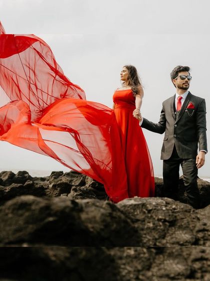 A powerful and stylish pre-wedding pose on the rocks. The red trail gown billows in the wind, creating a stunning contrast with the groom-to-be's suit.