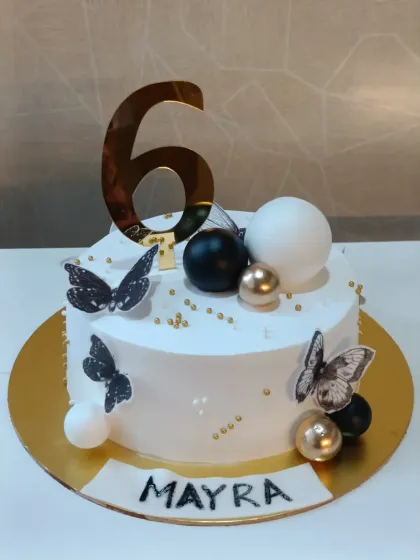 A modern and chic cake for a 6th birthday. The clean white design is accented with black and gold butterflies and spheres for a stylish touch.