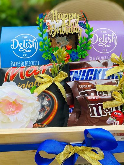 A close-up of the birthday hamper, showing the custom 'Happy Birthday' cake topper nestled among gourmet cookies and a variety of popular chocolates.