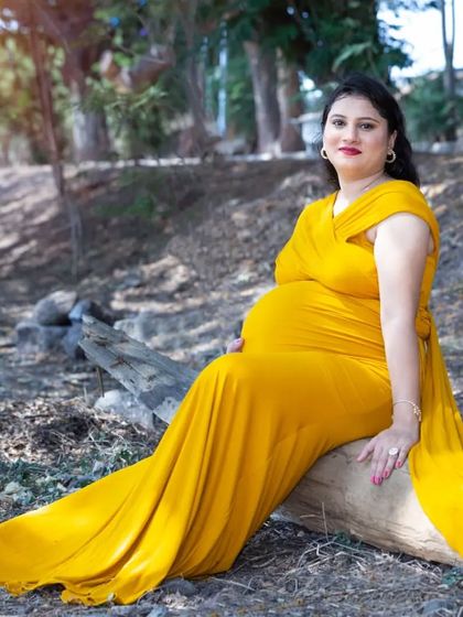A peaceful moment sitting on a log in the woods. The long, flowing yellow gown drapes beautifully, creating a classic and elegant maternity portrait.
