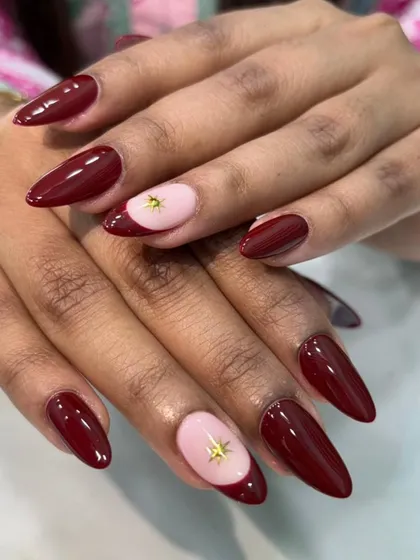 A chic and sophisticated color combination. This design pairs deep maroon stiletto nails with a pale pink accent nail, featuring a simple gold star embellishment.