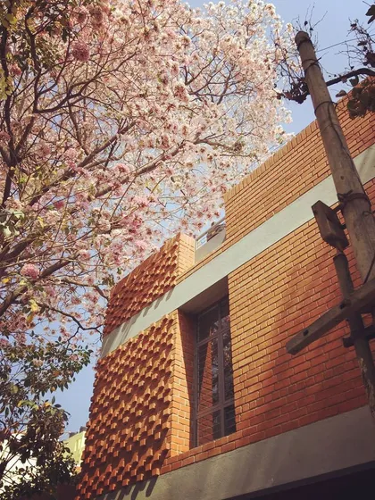 The warmth of exposed brickwork is timeless. This photo of our completed residence in HSR, Bangalore, captures how the textured facade interacts with the natural beauty of a blooming Tabebuia tree, grounding the modern structure in its environment.