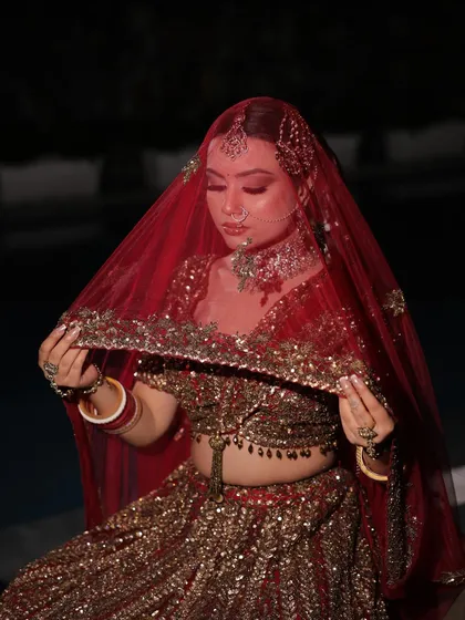 The quintessential bridal pose with the dupatta veil. This shot highlights the heavy embroidery on the border of the veil, perfectly complementing the rich work on the lehenga.