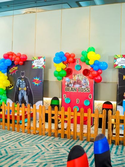 A variety of game stalls for every hero. This setup includes multiple themed booths like bean toss and other carnival-style games, each featuring a different superhero like Batman and Black Widow.