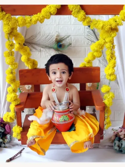 A joyful baby boy in our Krishna swing setup, holding a pot of 'butter'. The vibrant colors and fun props make these sessions a delight.