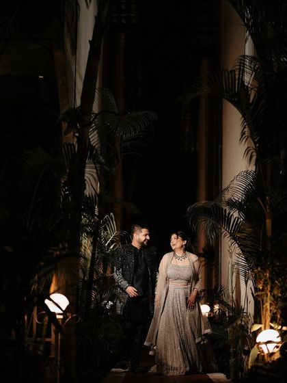 A quiet moment amidst the celebration. This shot captures the couple walking through the resort at night, the lush palms and soft lighting creating a romantic, cinematic scene.