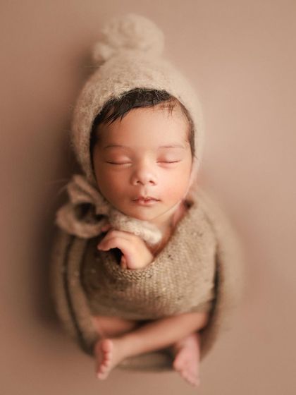 Cuteness in a cozy bonnet. This simple, elegant portrait in neutral tones focuses on the baby's perfect, sleepy face and tiny hands.