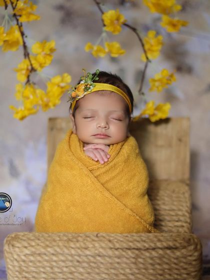 A simple and sweet portrait of a newborn swaddled in yellow, sitting upright in a small jute chair, looking like a little ray of sunshine.