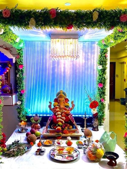 A square-shaped mandap made of lush green garlands and pink roses. The crystal chandelier and blue-lit backdrop add a touch of modern glamour to the traditional setup.