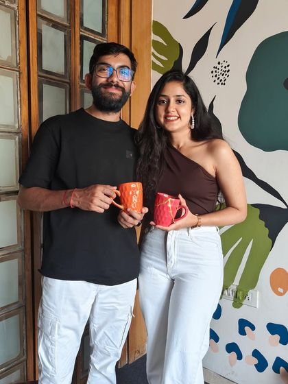 A couple holding up the matching mugs they decorated. A simple, sweet, and creative date idea.
