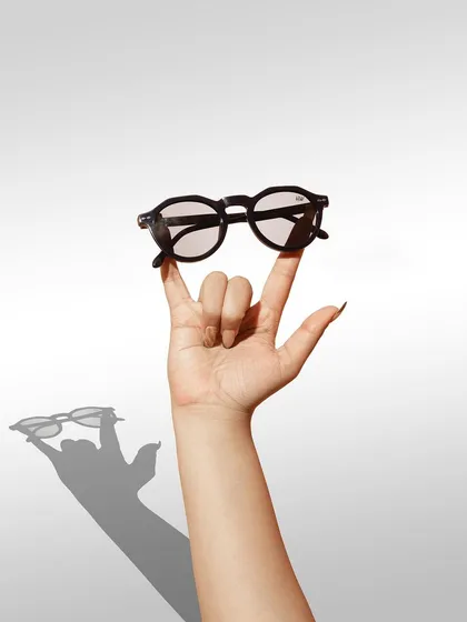 A playful shot of a hand making a "rock on" gesture while balancing sunglasses. The strong shadow and fun pose give the product a cool, edgy, and youthful vibe.
