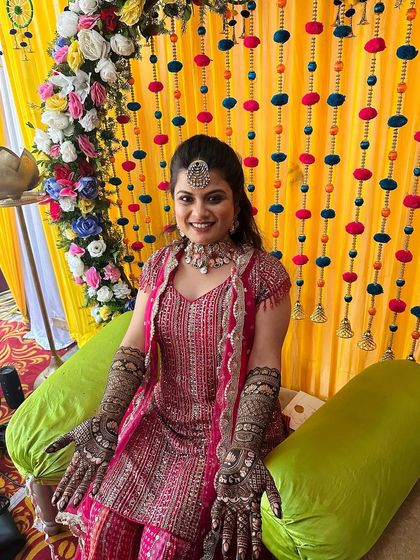 A smiling bride proudly displaying her intricate mehndi against a festive backdrop.