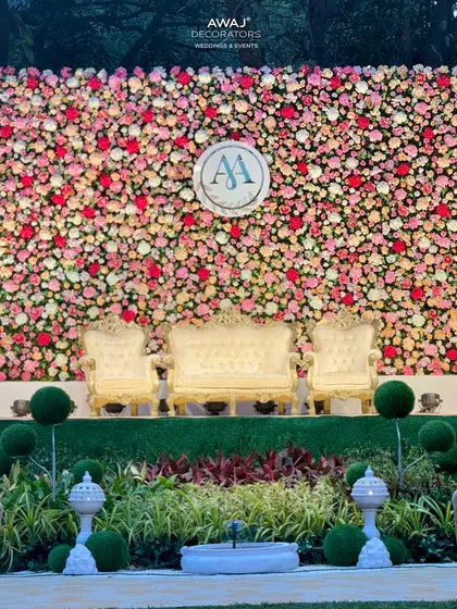 The complete wedding stage with its magnificent flower wall, ornate gold and cream furniture, and manicured topiary, creating a royal garden feel.