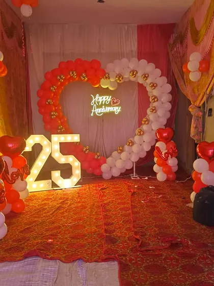 A grand 25th anniversary party setup. This decoration features a large heart-shaped balloon arch, light-up numbers, and smaller balloon pillars for a complete look.