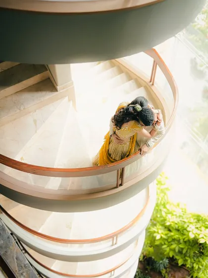 A creative high angle shot of a couple embracing on a spiral staircase, using the architecture to frame them in a unique and artistic way.