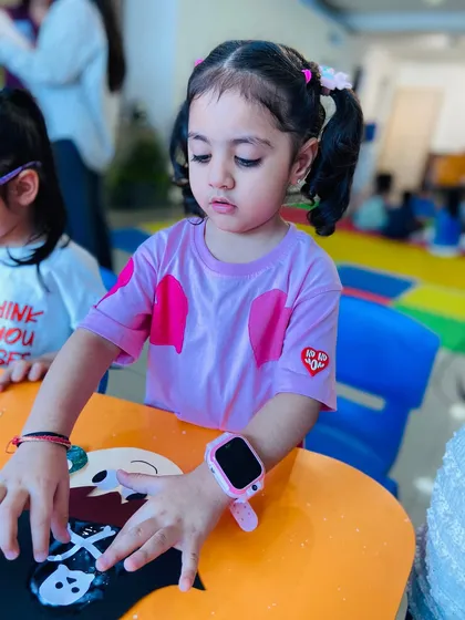 A young girl carefully works on her craft, her colorful watch adding a personal touch to the scene.