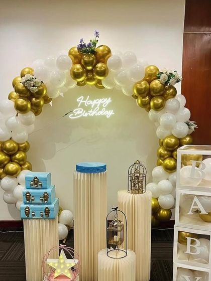 A clean and classic white and gold theme. This arrangement features a balloon arch, a neon sign, and various props like decorative trunks, birdcages, and 'ABC' blocks, offering a versatile backdrop.