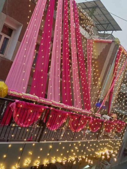 The warm glow of fairy lights adds a dreamy touch to this pink-themed exterior decoration at dusk, highlighting the beautiful draping work.