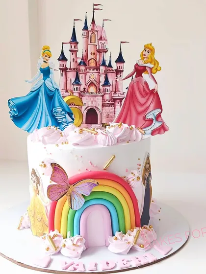A fairytale castle cake featuring Disney princesses Cinderella and Aurora. The design includes a colorful rainbow and butterfly, creating a magical scene for a princess-themed party.