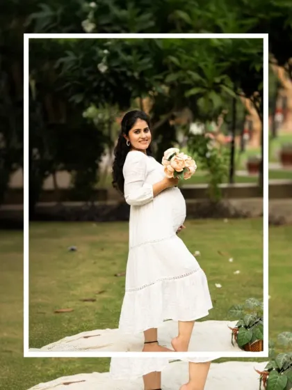 A beautiful full-length portrait of an expecting mother in a white dress, holding a bouquet of flowers during her outdoor session.