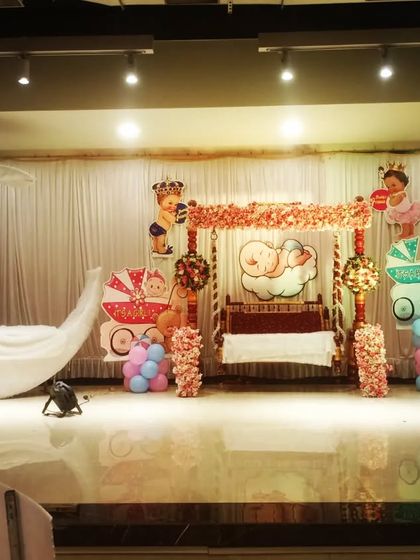 A traditional 'rukhwat' or 'otibharan' setup for a baby shower. The stage includes a decorated swing and a lighted moon prop, ready for the ceremony.