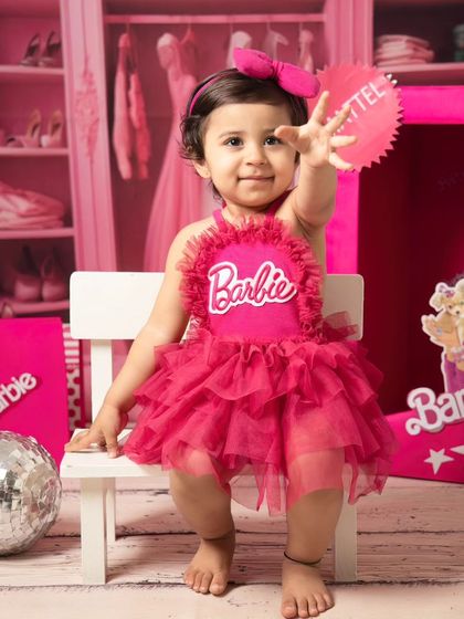 A playful moment captured as this little girl in a Barbie dress reaches out towards the camera with a happy expression.