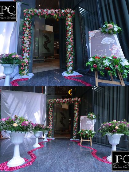 The entrance to the baby shower, featuring a floral archway and a welcome sign. A path of scattered rose petals leads guests into the celebration, creating a feeling of love and anticipation.