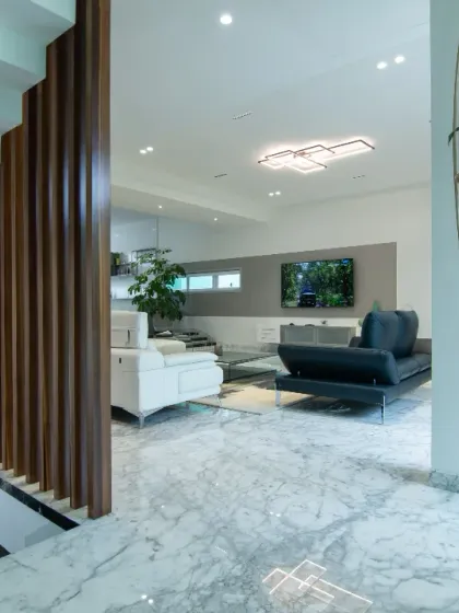 A view from the upper level into the main living area, showcasing the interplay of different materials. Polished marble floors, a wooden slatted screen, and comfortable, modern furniture come together to create a cohesive and sophisticated interior.