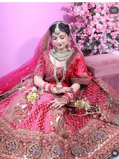 A beautiful bride seated in a magnificent pink and red dual-tone lehenga. This shot highlights the expansive flare of the skirt and the detailed craftsmanship of both the outfit and the matching emerald-accented bridal jewellery.