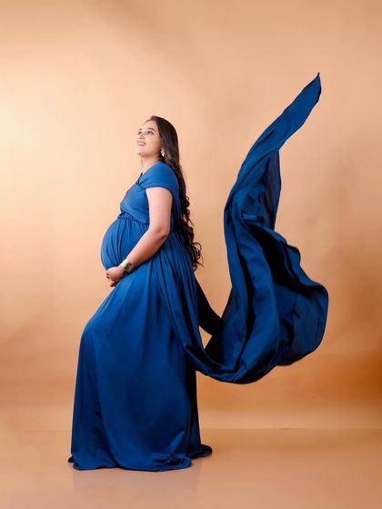 A classic maternity pose with a twist. The flowing blue fabric of the gown is tossed to the side, adding a sense of motion and elegance to this beautiful side profile.