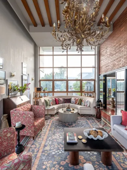 A double-height living room in Dhaka feels open and airy, thanks to the massive window wall. I used a dramatic, leaf-like chandelier and a mix of floral and solid fabrics to ground the space and add layers of interest, making it feel both impressive and comfortable.
